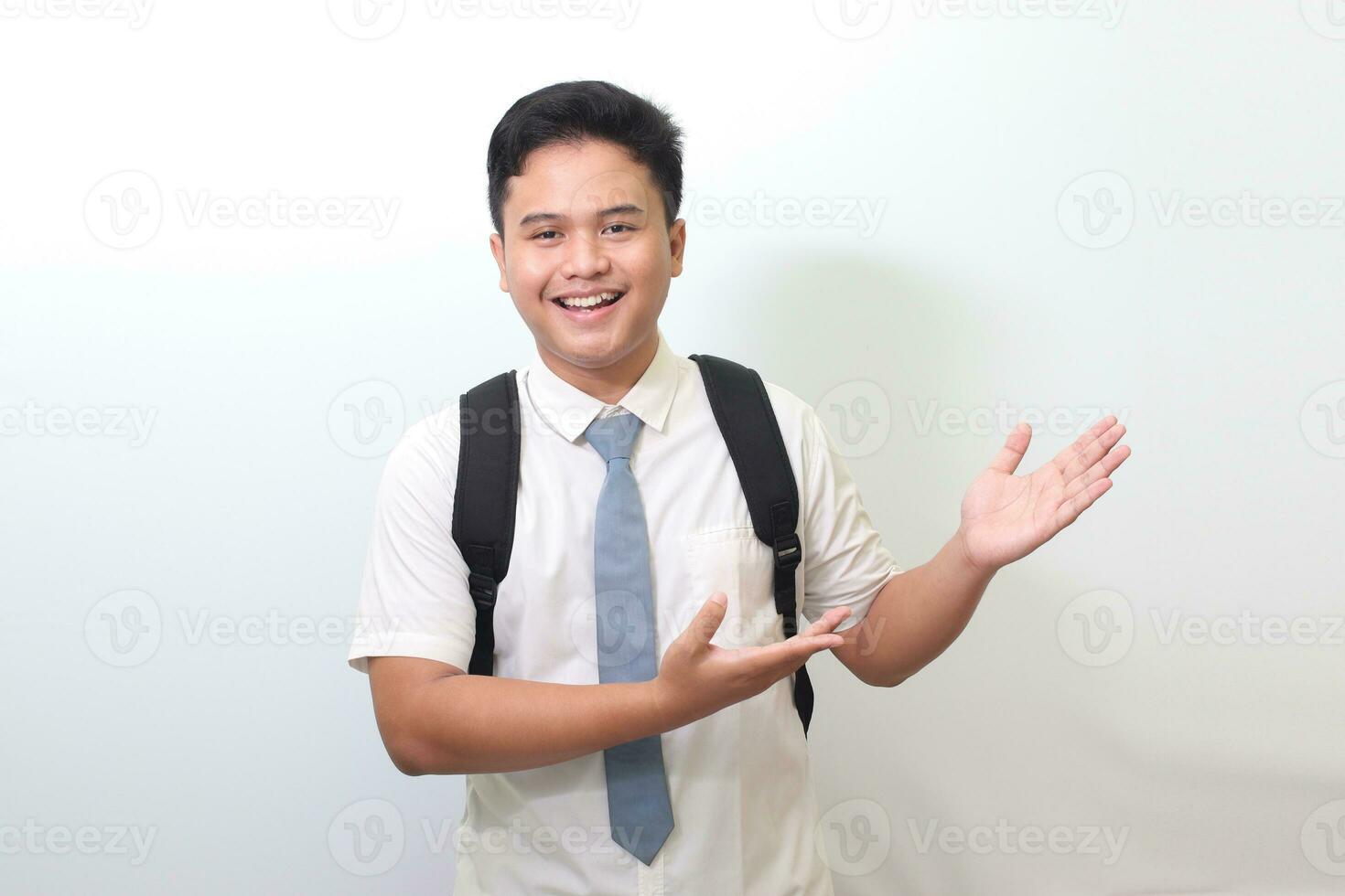 Indonesian senior high school student wearing white shirt uniform with gray tie showing product, pointing at something and smiling. Isolated image on white background photo