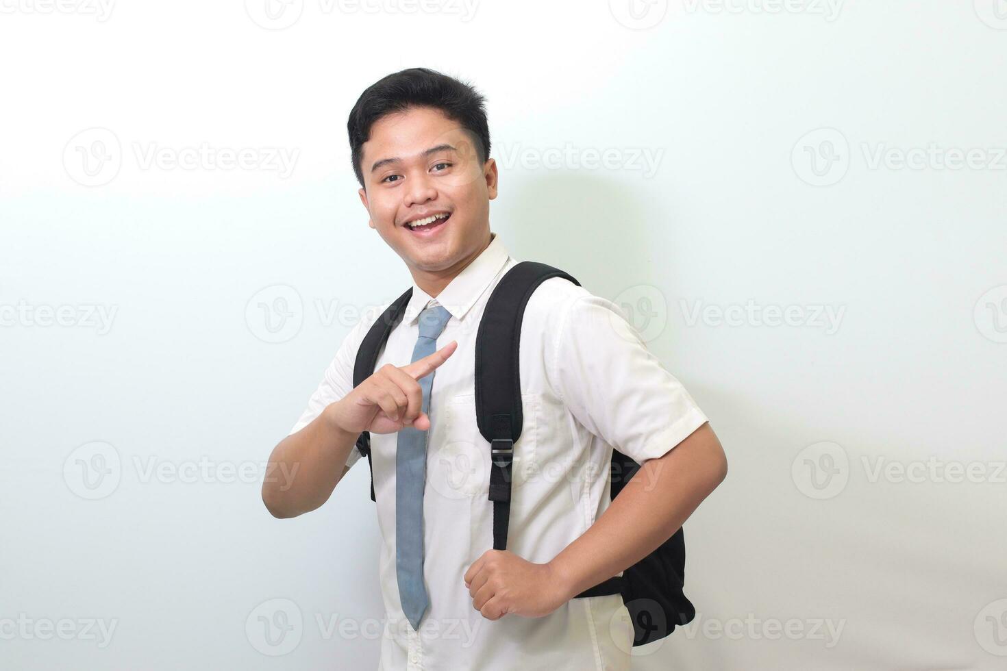 Indonesian senior high school student wearing white shirt uniform with gray tie showing product, pointing at something and smiling. Isolated image on white background photo