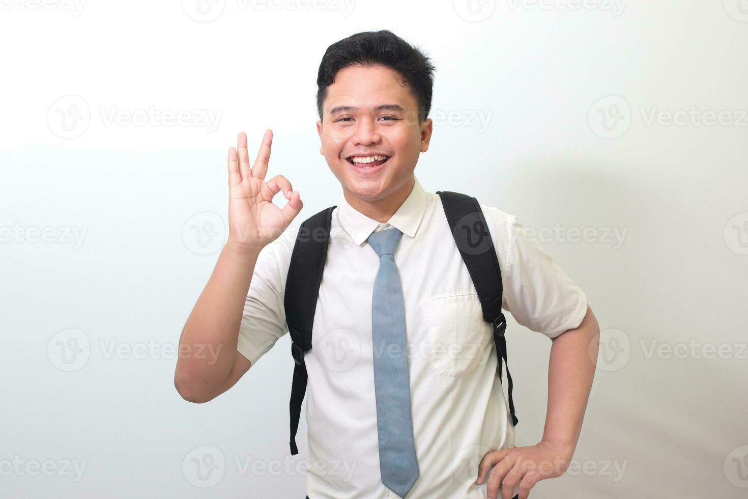 Indonesian senior high school student wearing white shirt uniform with gray tie showing ok hand gesture and smiling looking at camera. Isolated image on white background photo