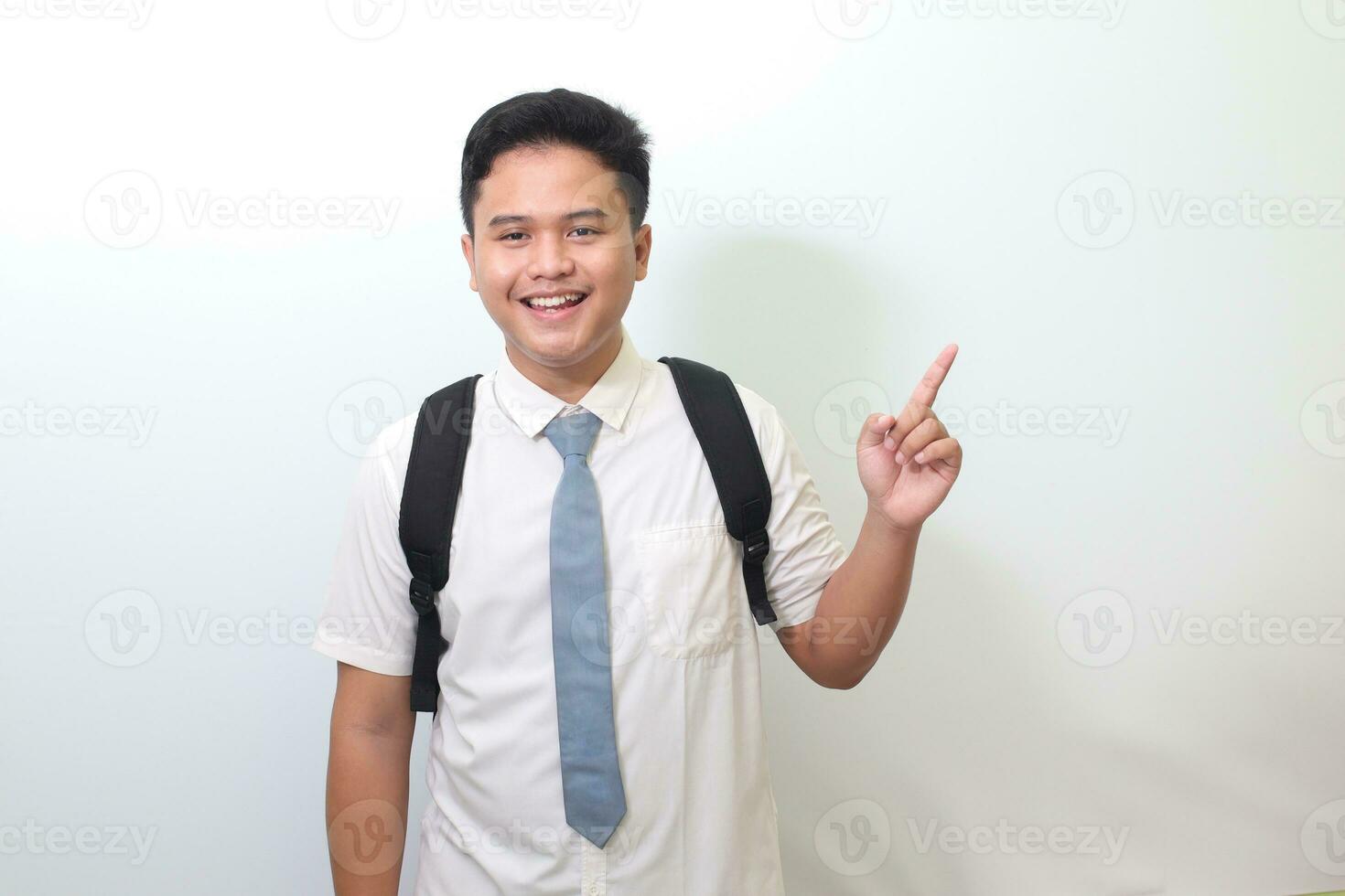 indonesio mayor alto colegio estudiante vistiendo blanco camisa uniforme con gris Corbata demostración producto, señalando a alguna cosa y sonriente. aislado imagen en blanco antecedentes foto