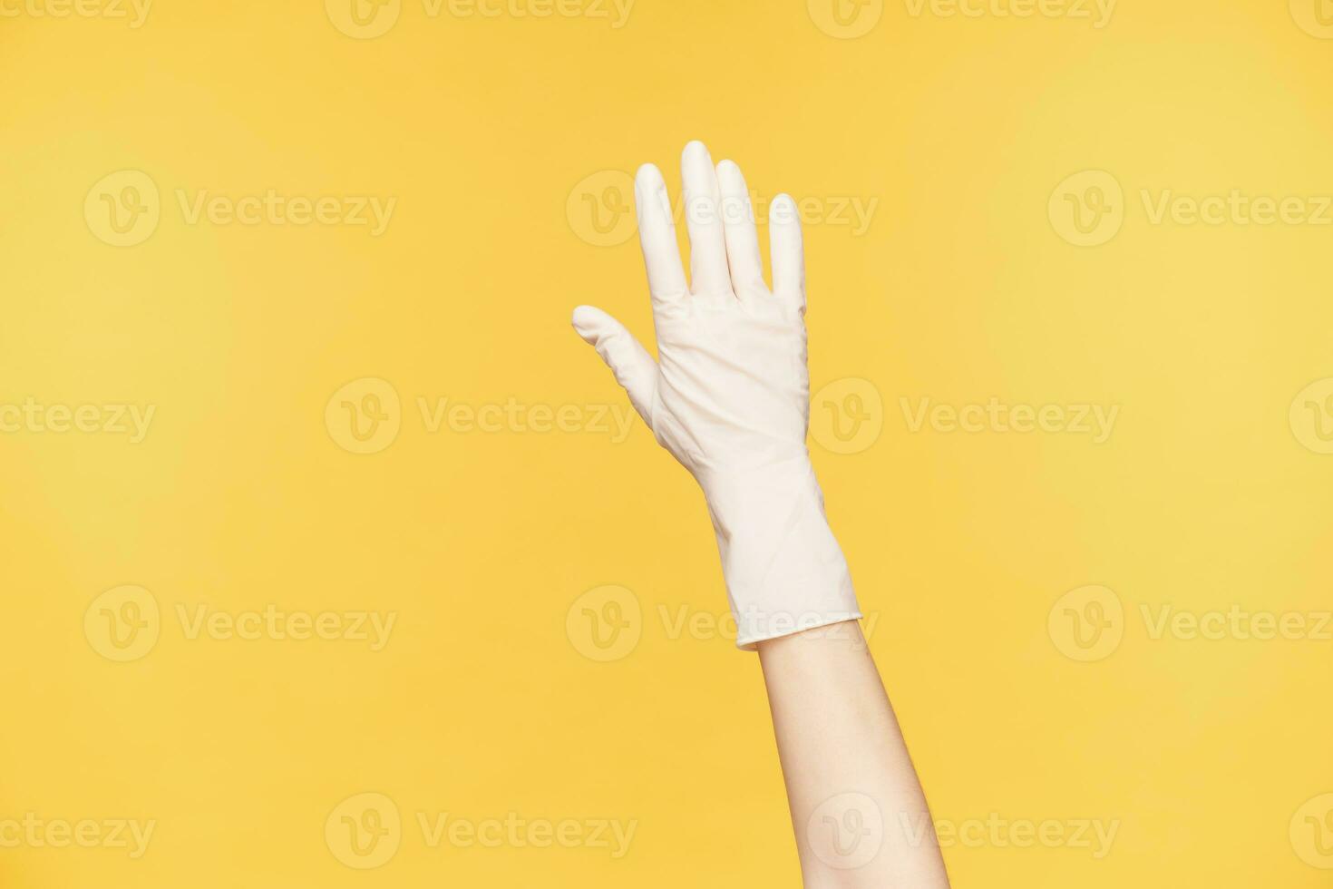 Close-up of raised hand in white rubber glove posing over orange background, keeping all fingers separately. Preparing for spring cleaning of house photo