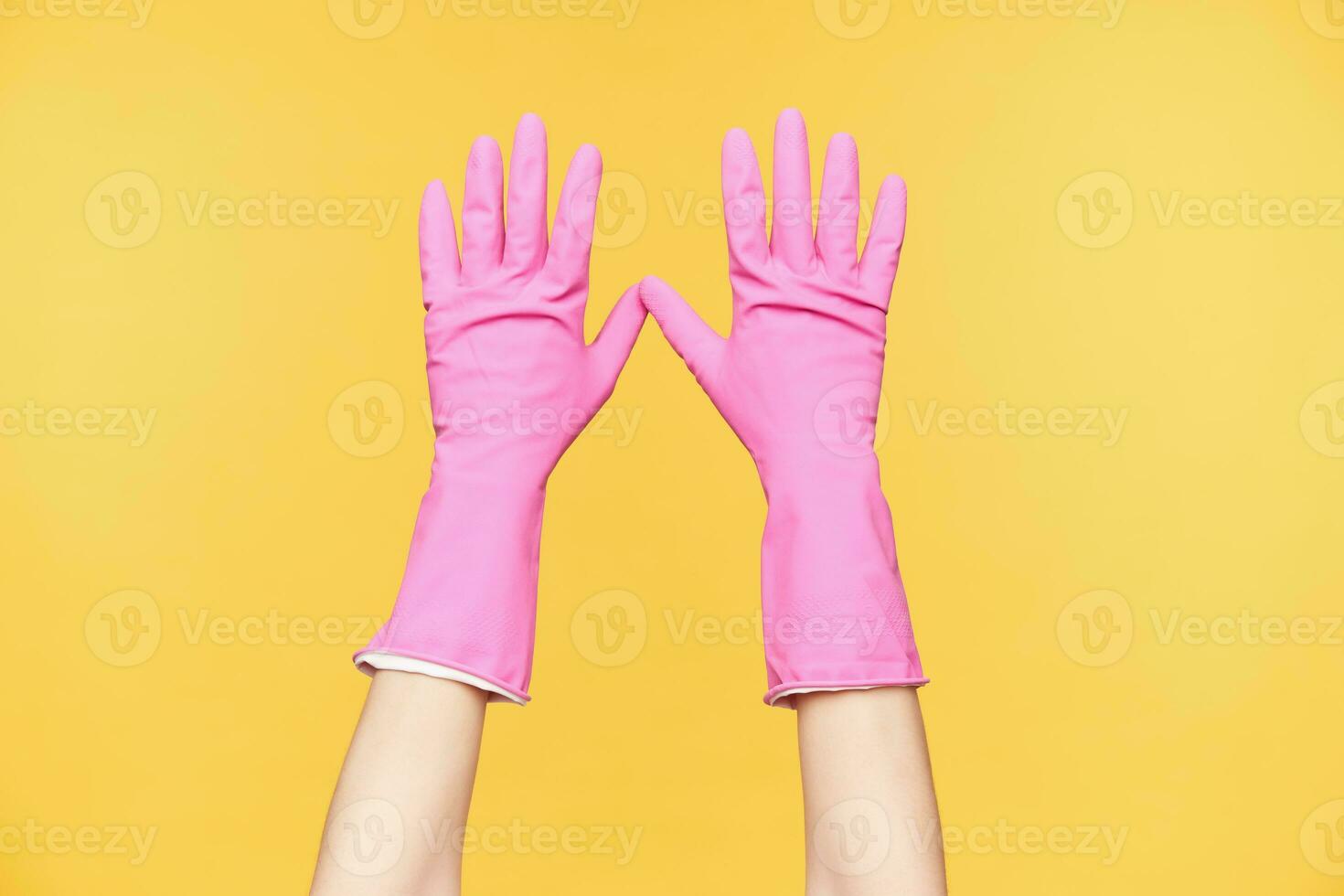 Front view of raised hands in red rubber gloves being isolated against orange background, keeping all fingers separately. Human hands and body concept photo