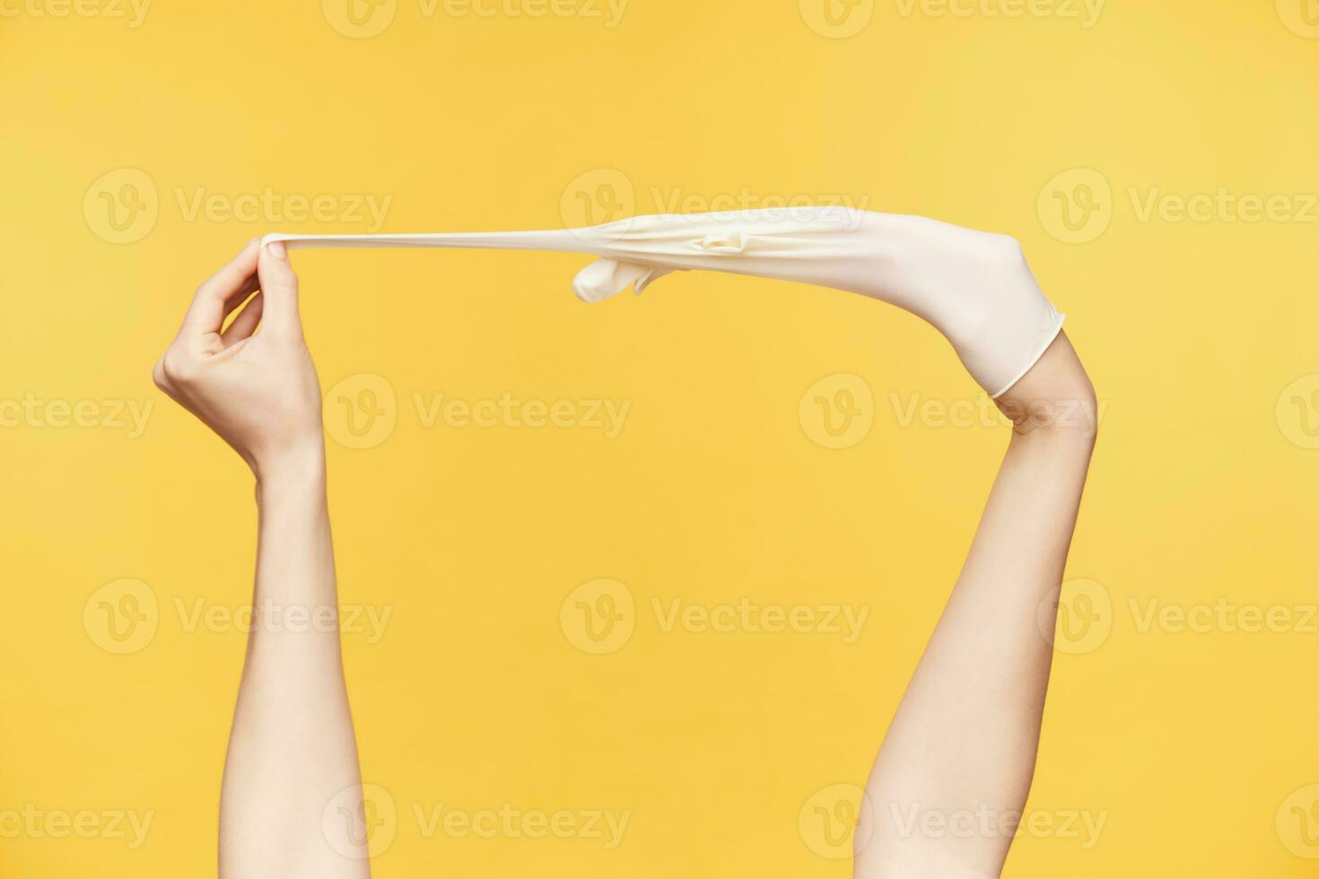 recortado Disparo de joven femenino manos siendo elevado blanco tomando fuera caucho guantes, posando terminado naranja antecedentes. limpieza y humano manos concepto foto