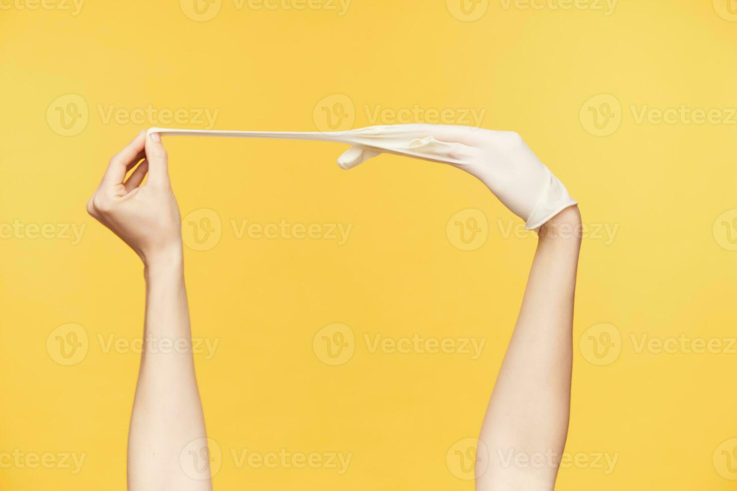 Studio photo of young woman's hands posing over orange background, one hand pulling middle finger while taking out white rubber glove. Human hands concept