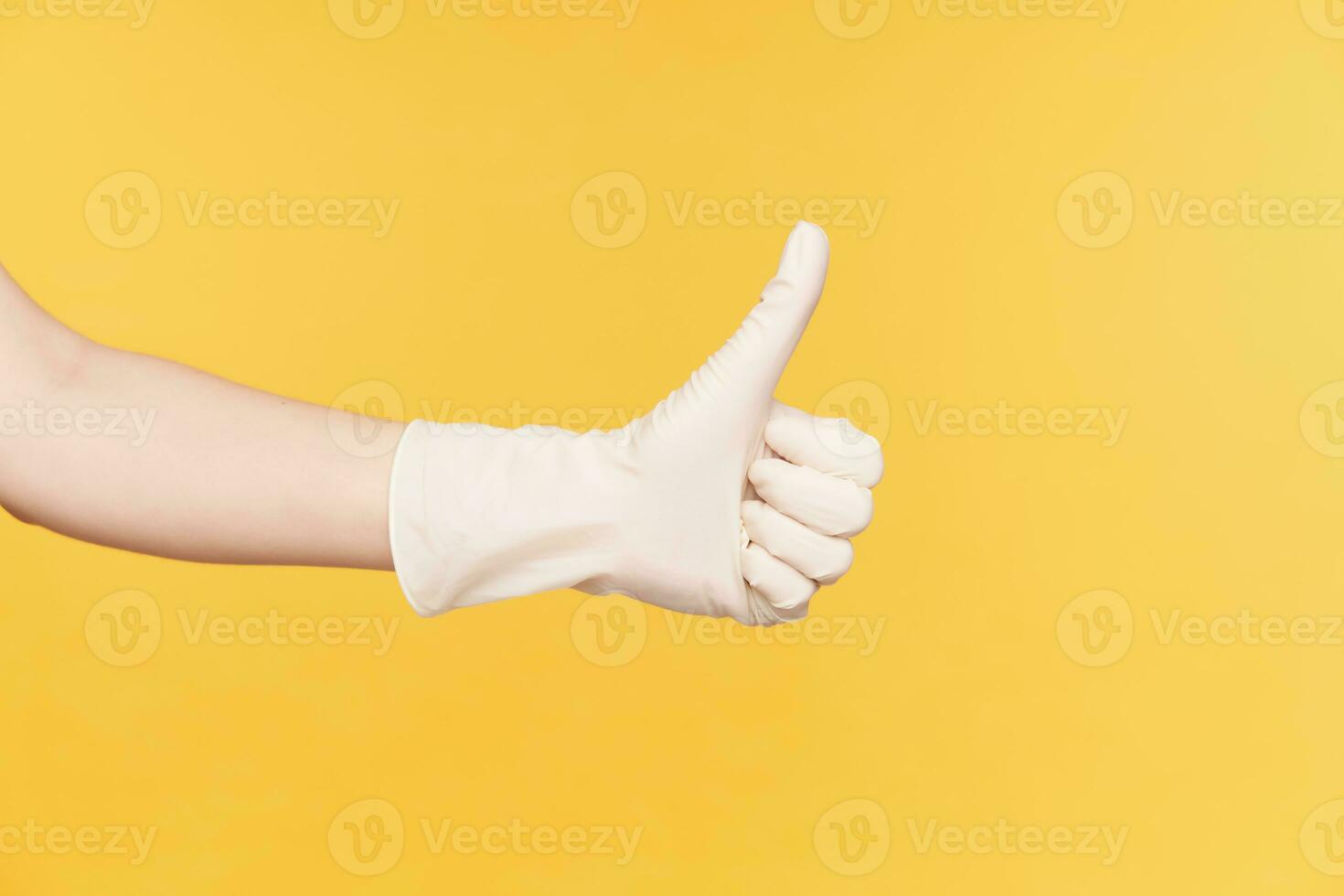 Horizontal photo of raised hand in white gloves showing thumb while demonstrating well done sign, isolated over orange background. Body language and gesturing concept