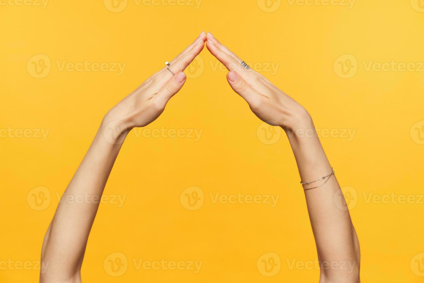 Studio photo of pretty well-groomed hands of young female folding togather while imitating roof of house, isolated over yellow background. Woman hands concept
