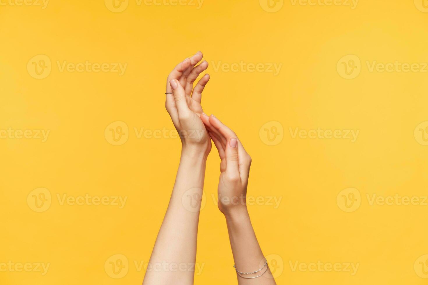 Horizontal photo of young pretty hands of woman touching each other gently while being isolated over yellow background. Body signs and language concept