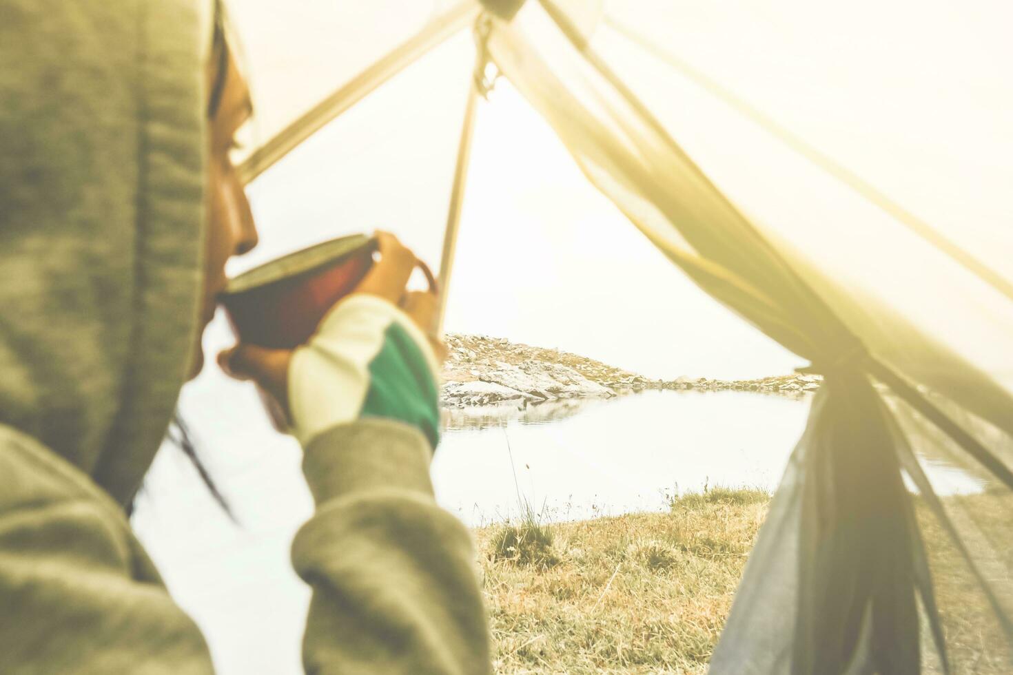 Close up thoughtful female caucasian drink hot beverage coffee in tent by the lake enjoy panorama in nature enjoy scenic mountains panorama in early morning sunrise solo photo