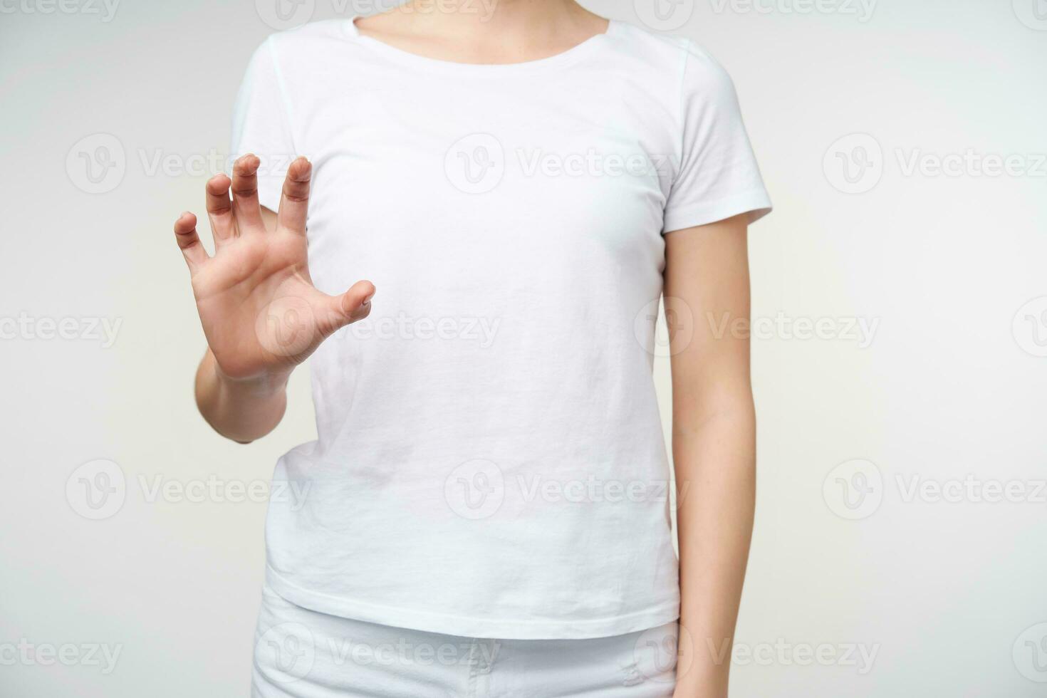 Studio photo of young female dressed in casual clothes keeping her hand raised while using sign language to show word photographer, standing over white background