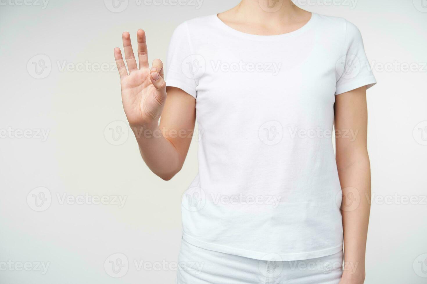 Studio shot of young woman showing raised hand while forming with fingers number nine using sing language, isolated aginst white background in casual wear photo