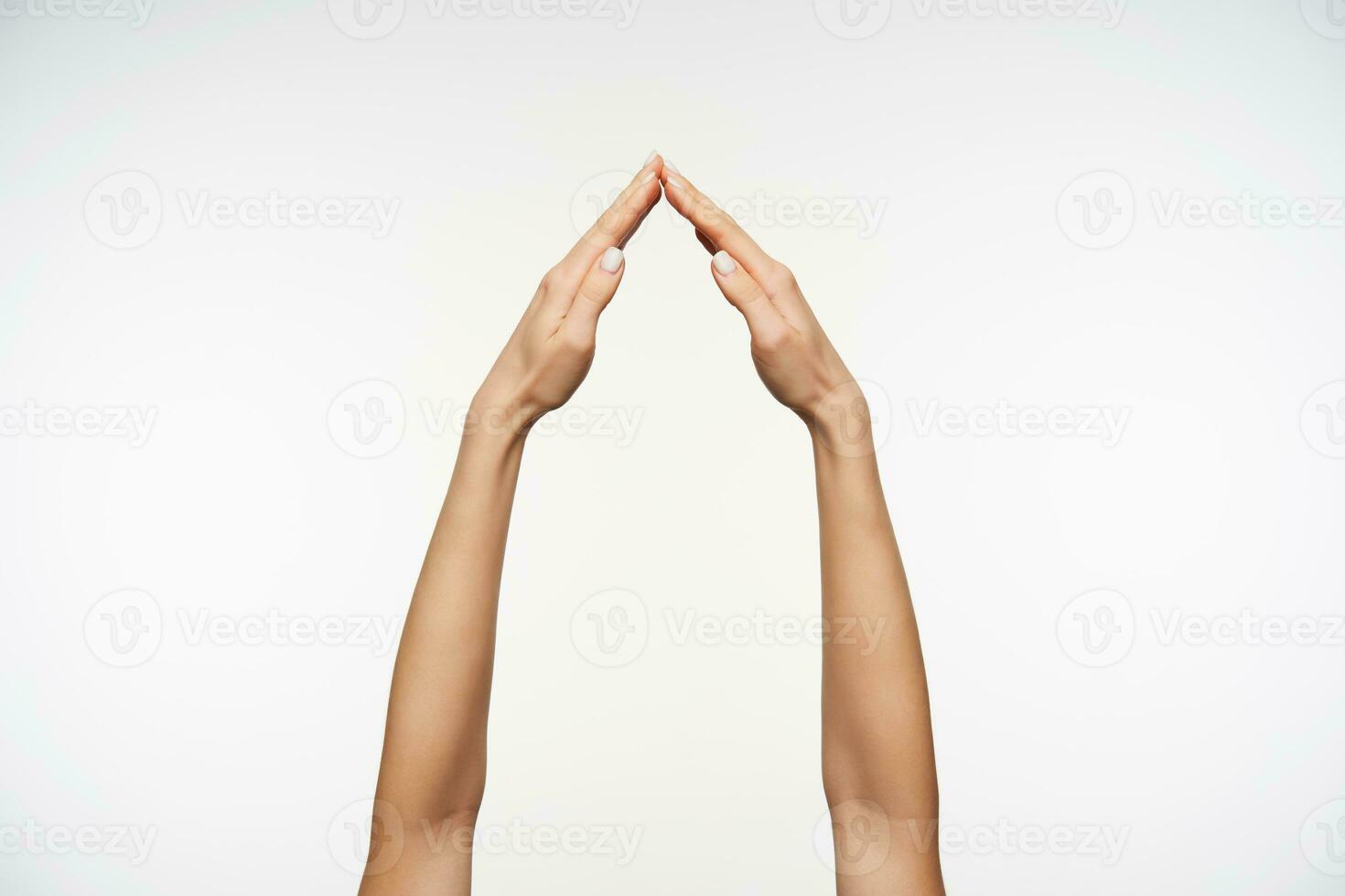 Elegant woman's hands being raised while posing over white background, folding house with palms while imitating home sign. Body language and gestures photo