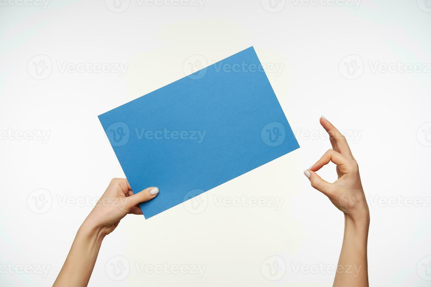 dos elevado joven mujer manos posando terminado blanco fondo, uno mano es participación azul sábana de papel y otro uno formando bien hecho firmar con dedos foto