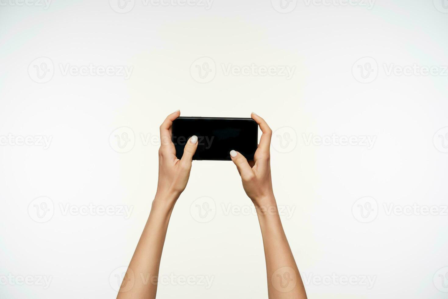 Horizontal shot of fair-skinned pretty woman's hands holding smartphone and moving fingers on screen while being isolated over white background photo