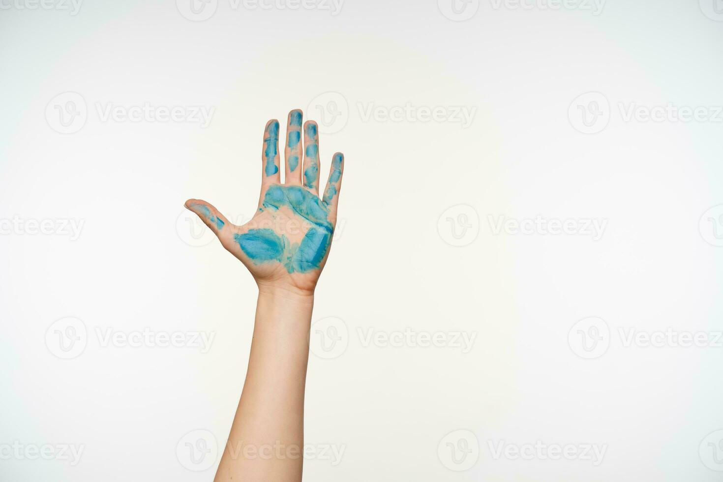 Indoor shot of raised female's arm demonstrating palm painted with blue colour while posing over white background. Body language and gestures concept photo