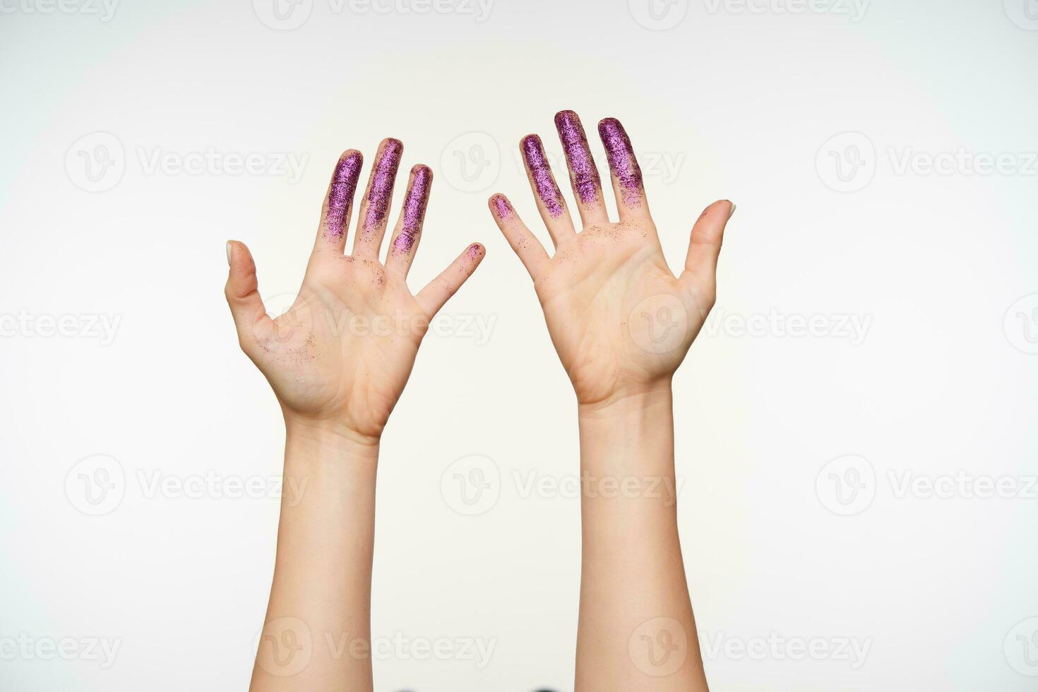 Studio photo of raised woman's hands being raised while showing palms and keeping all fingers with sparkles separately, posing over white background