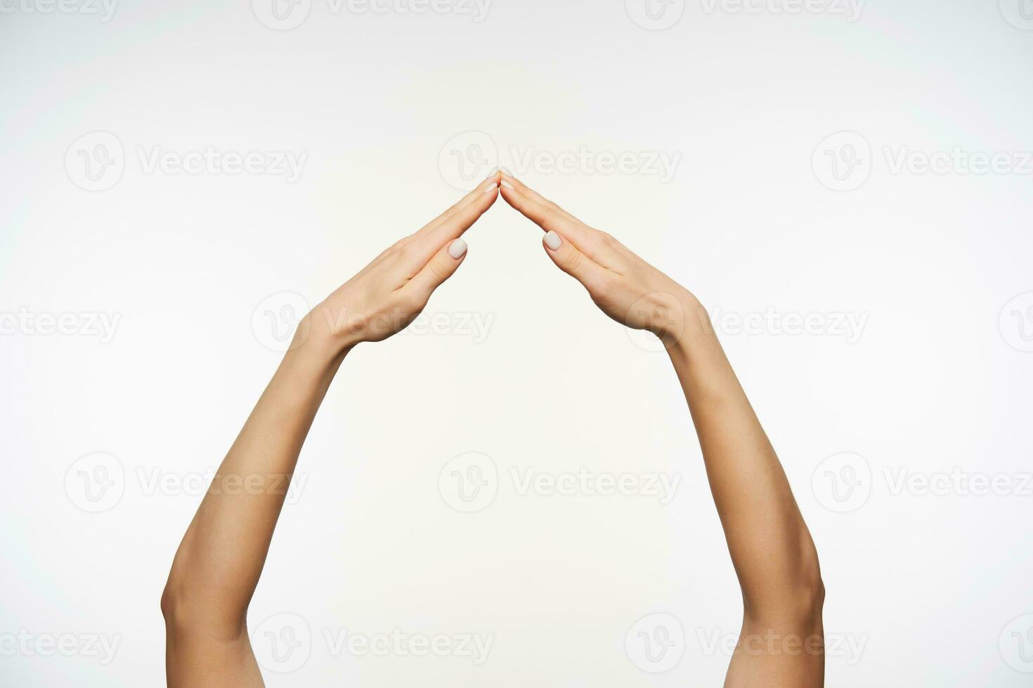 Raised female's pretty arms imitating house with folded palms while standing over white background, language hand symbol viewed from side view photo