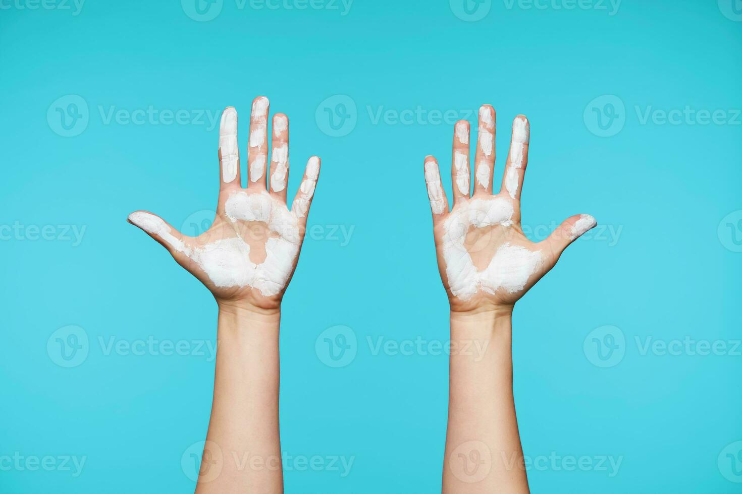 Two female's fair-skinned arms showing up raised palms with white paint while posing over white backgound. Human hands and gesturing concept photo