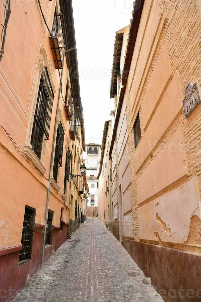 a narrow street with a few buildings and a cobblestone path photo