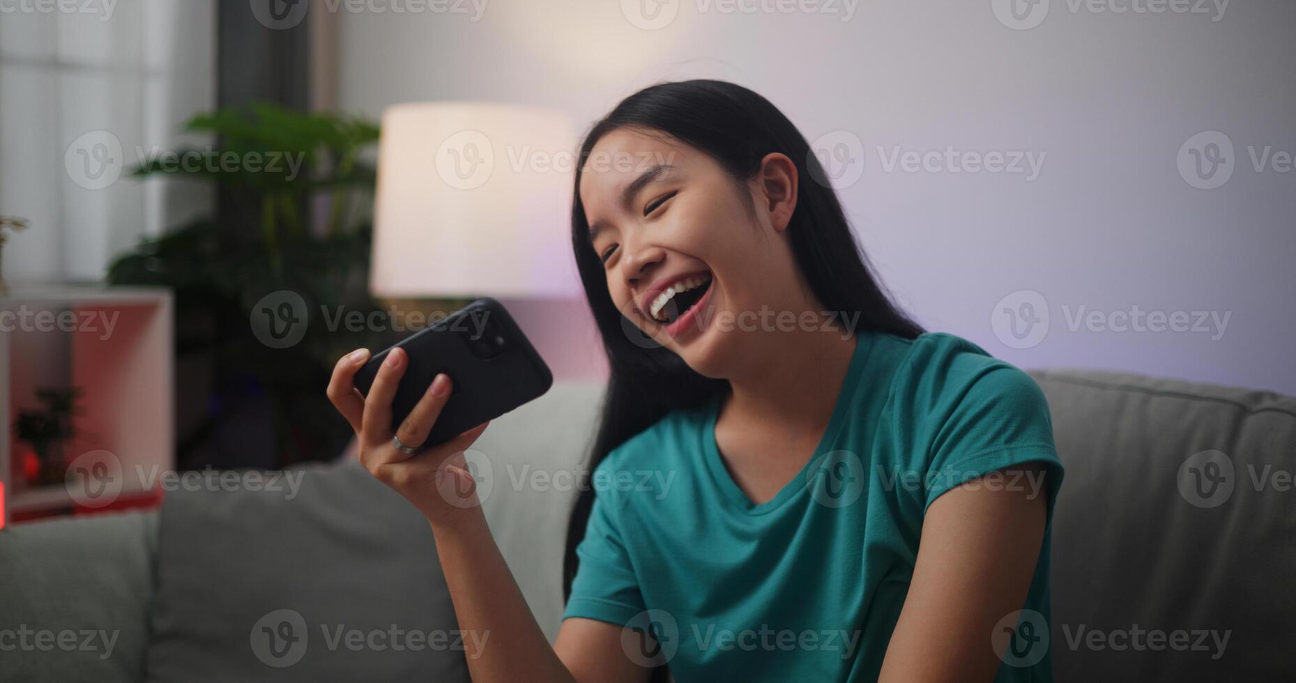 Portrait of Young Asian woman enjoys playing online esport games on smartphone sitting on sofa in the living room at home,Gamer lifestyle concept. photo