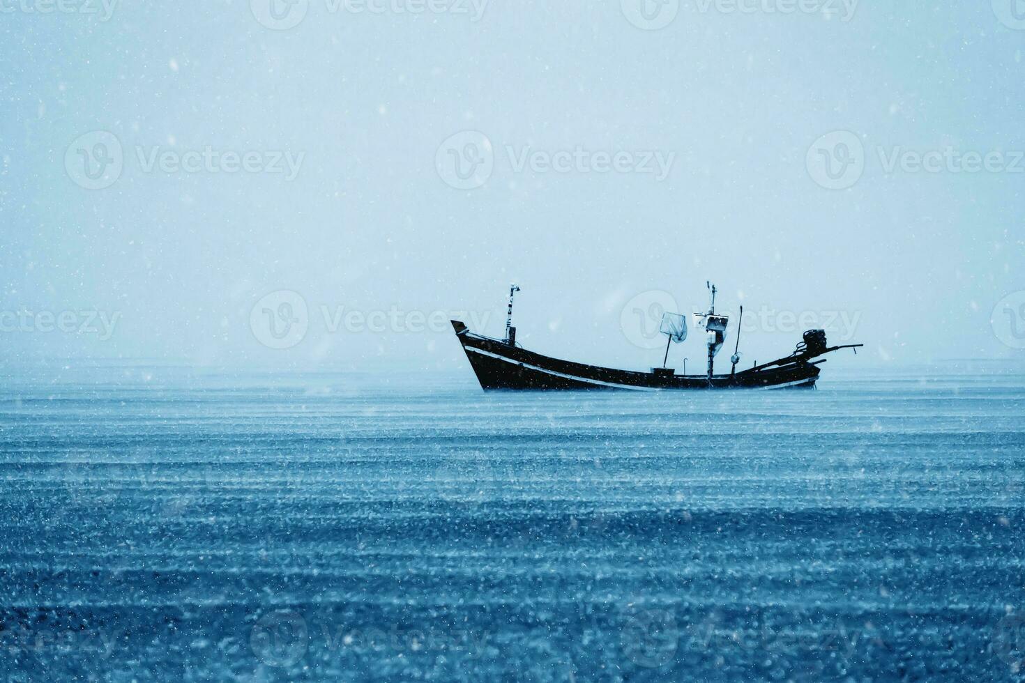 Fishing boat on the sea with snowfall in winter color tone. photo