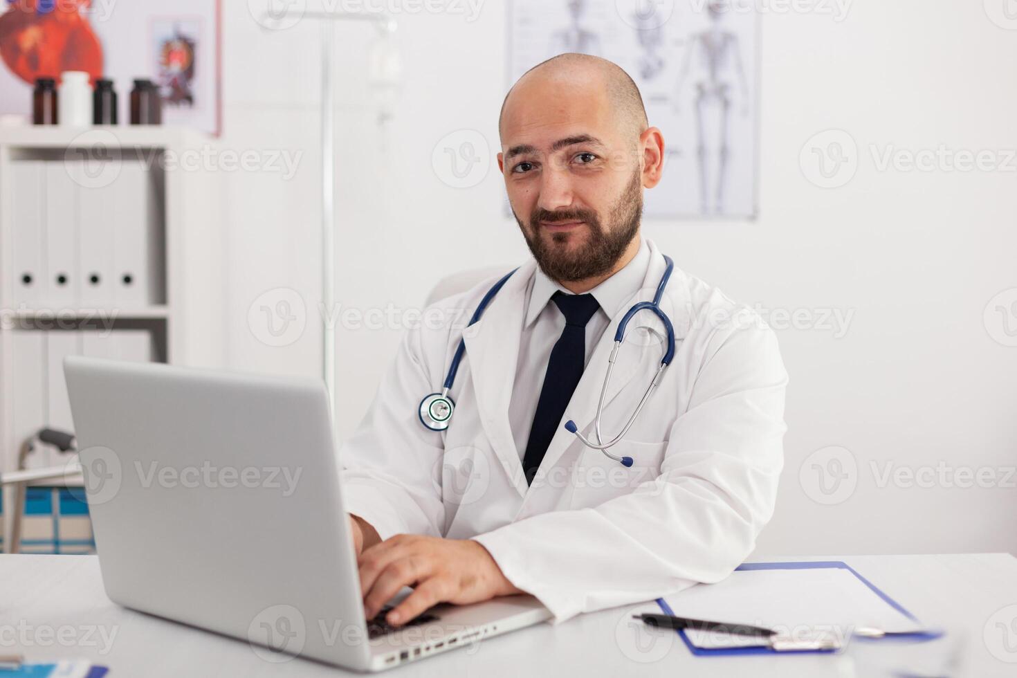 Portrait of specialist physician man looking into camera working in meeting conference room analyzing sickness expertise using laptop computer. Doctor prescribing pills medication healthcare treatment photo