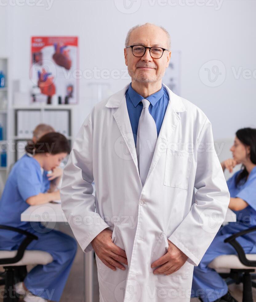 Therapist senior man standing in front of camera analyzing surgery symptom checking medical expertise. Hospital teamwork working in conference meeting room presenting disease treatment photo