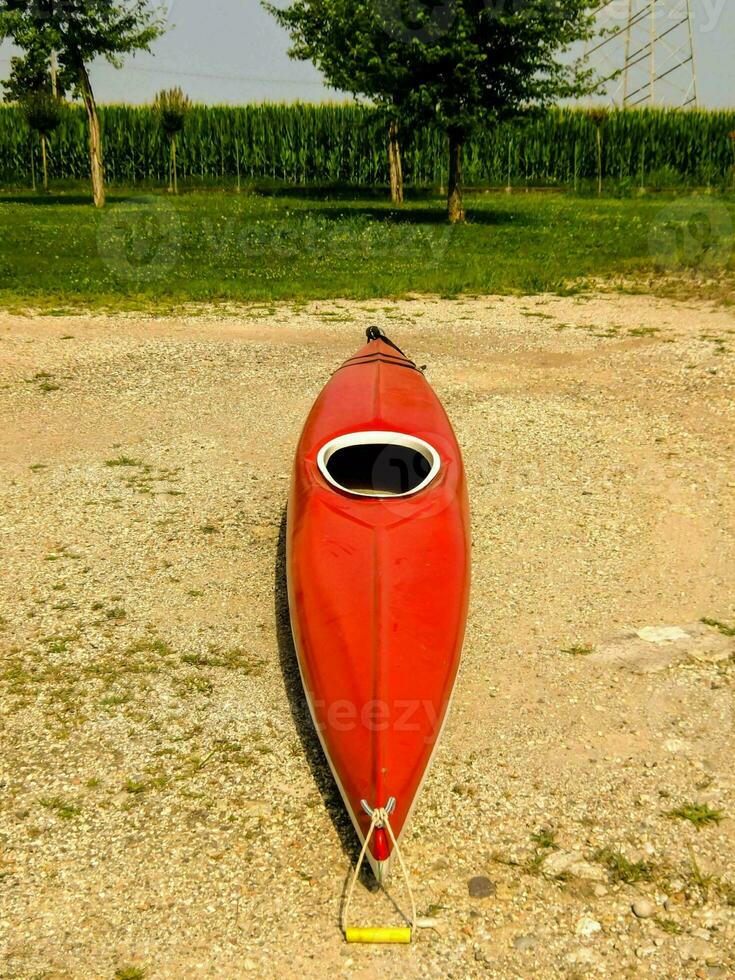 a red kayak sits on the ground in a gravel lot photo