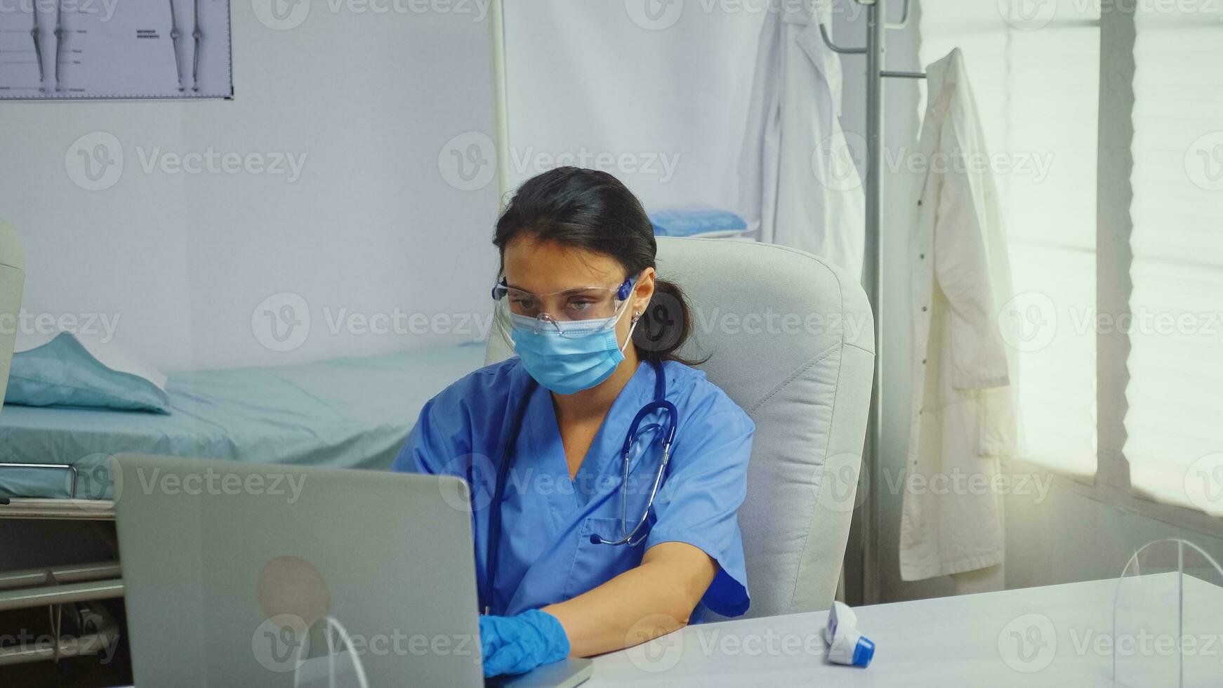 Nurse typing on laptop wearing medical gloves during coronavirus. Physician doctor specialist in medicine providing health care services consultation treatment examination in hospital cabinet photo