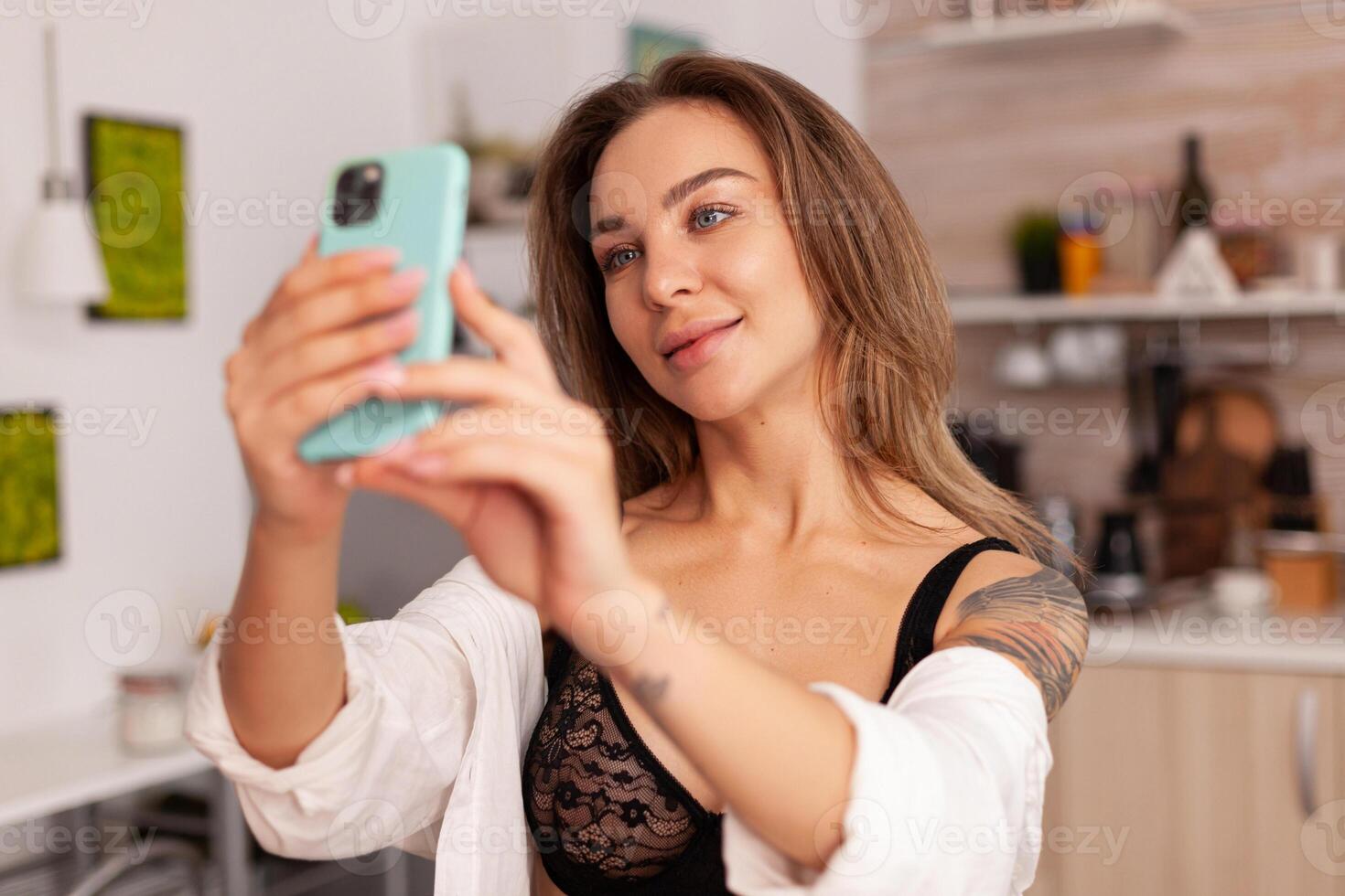 Woman ejoying taking photos during breakfast wearing sexy underwear. Seductive woman with tattoos using smartphone wearing temping lingerie in the morning.