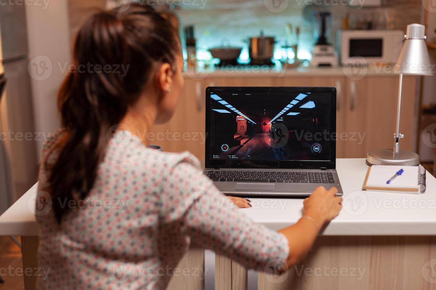 Lady playing games on laptop during night time during night time in home kitchen. Professional gamer playing online videop games on her personal computer. Geek cyber esport. photo
