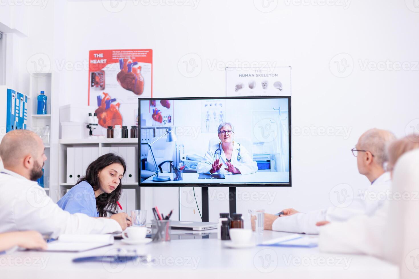 Group of doctors discussing with expert during video conference from hospital meeting room. Medicine staff using internet during online meeting with expert doctor for expertise. photo