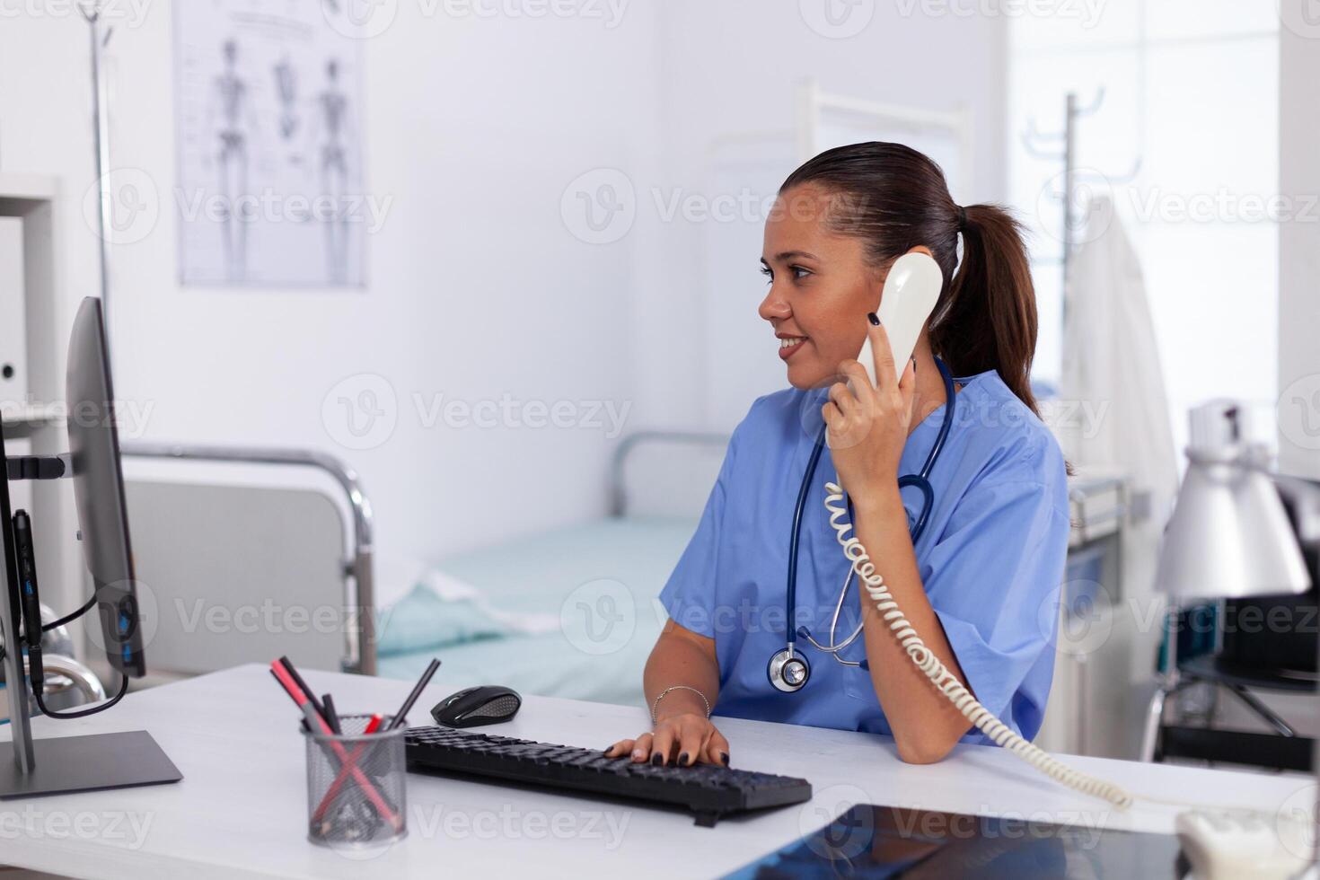 Medical nurse talking with patient on the phone about diagnosis. Health care physician sitting at desk using computer in modern clinic looking at monitor. photo