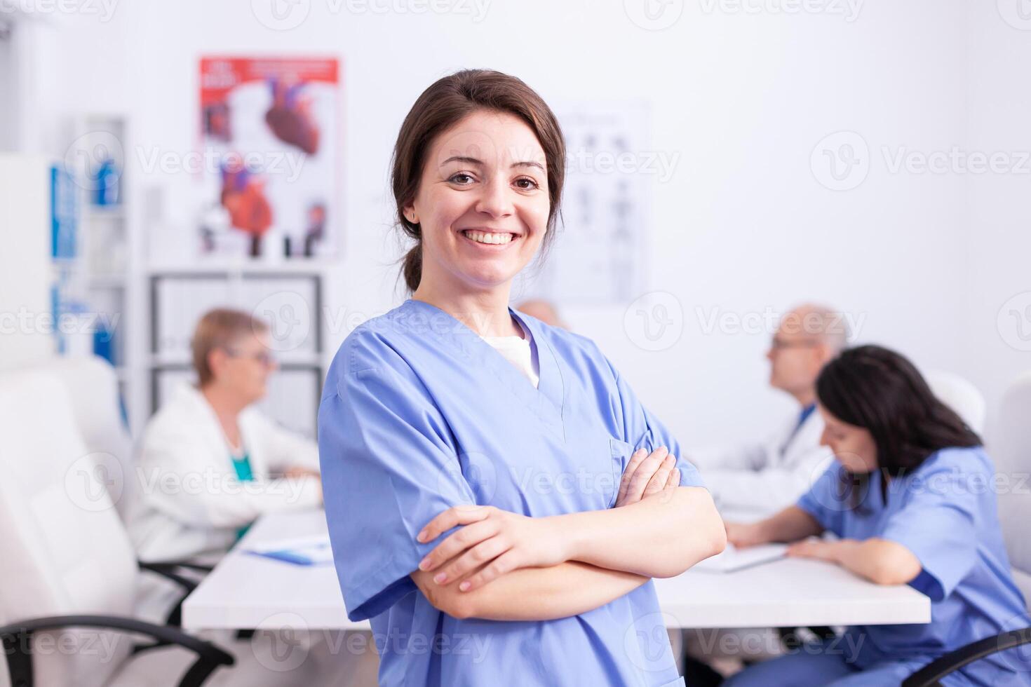 Young nurse wearing medical uniform in hospital conference room smiling at camera. Friendly medical practitioner in clinic meeting room, robe, specialist. photo
