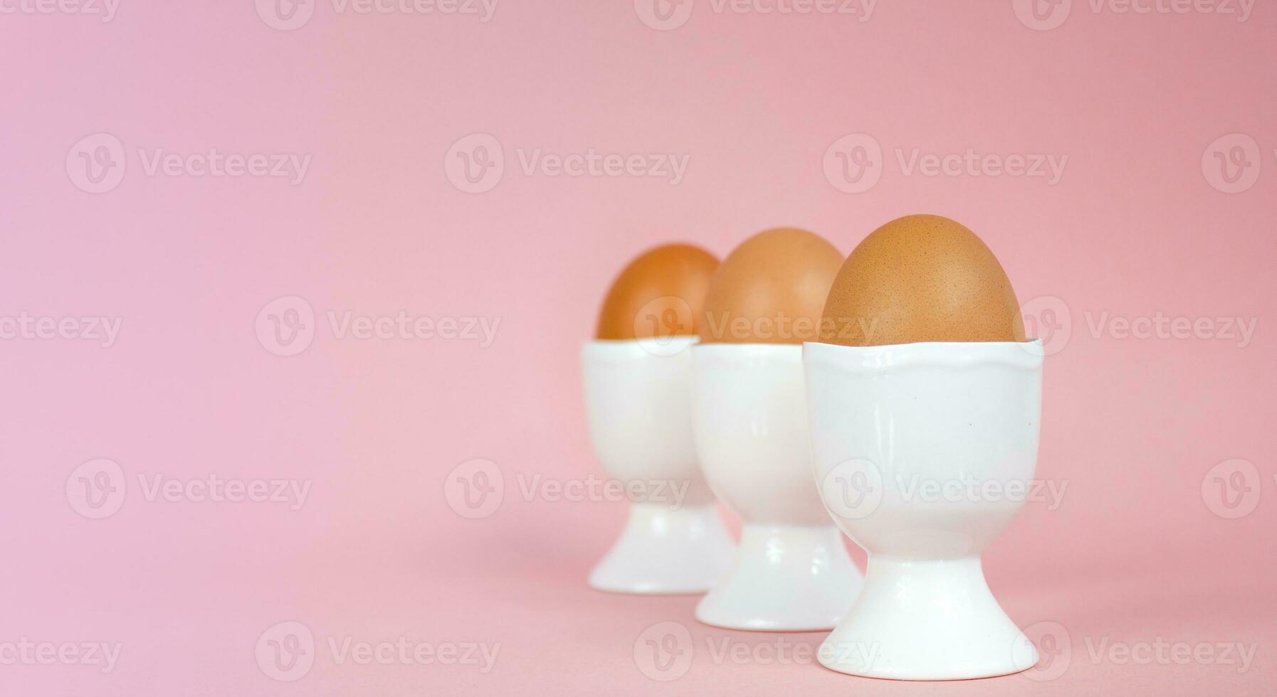 Eggs in egg cups on a pink background. Easter composition with copy space. photo