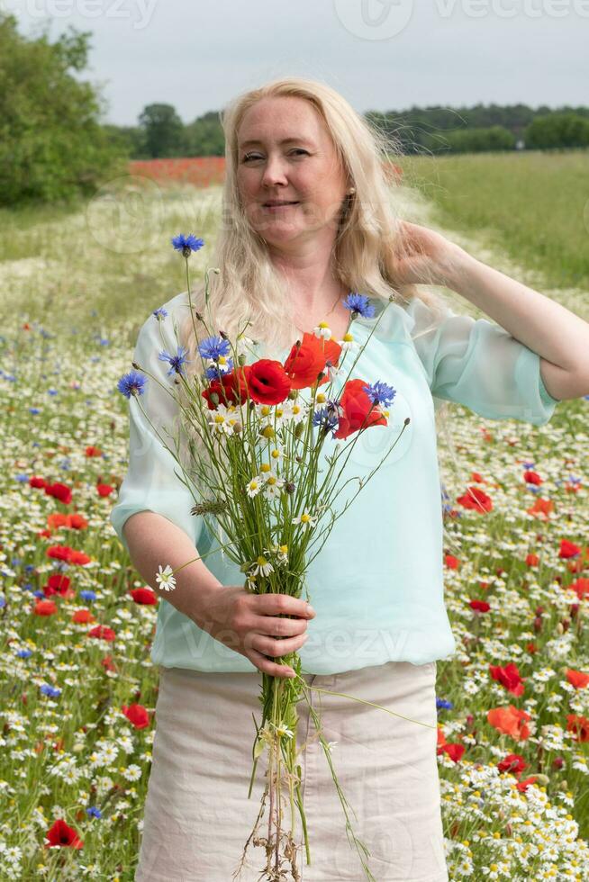 hermosa de edad mediana rubia mujer soportes entre un floración campo de amapolas foto