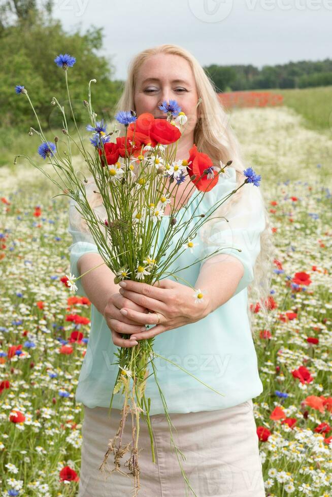 beautiful middle-aged blonde woman stands among a flowering field of poppies photo