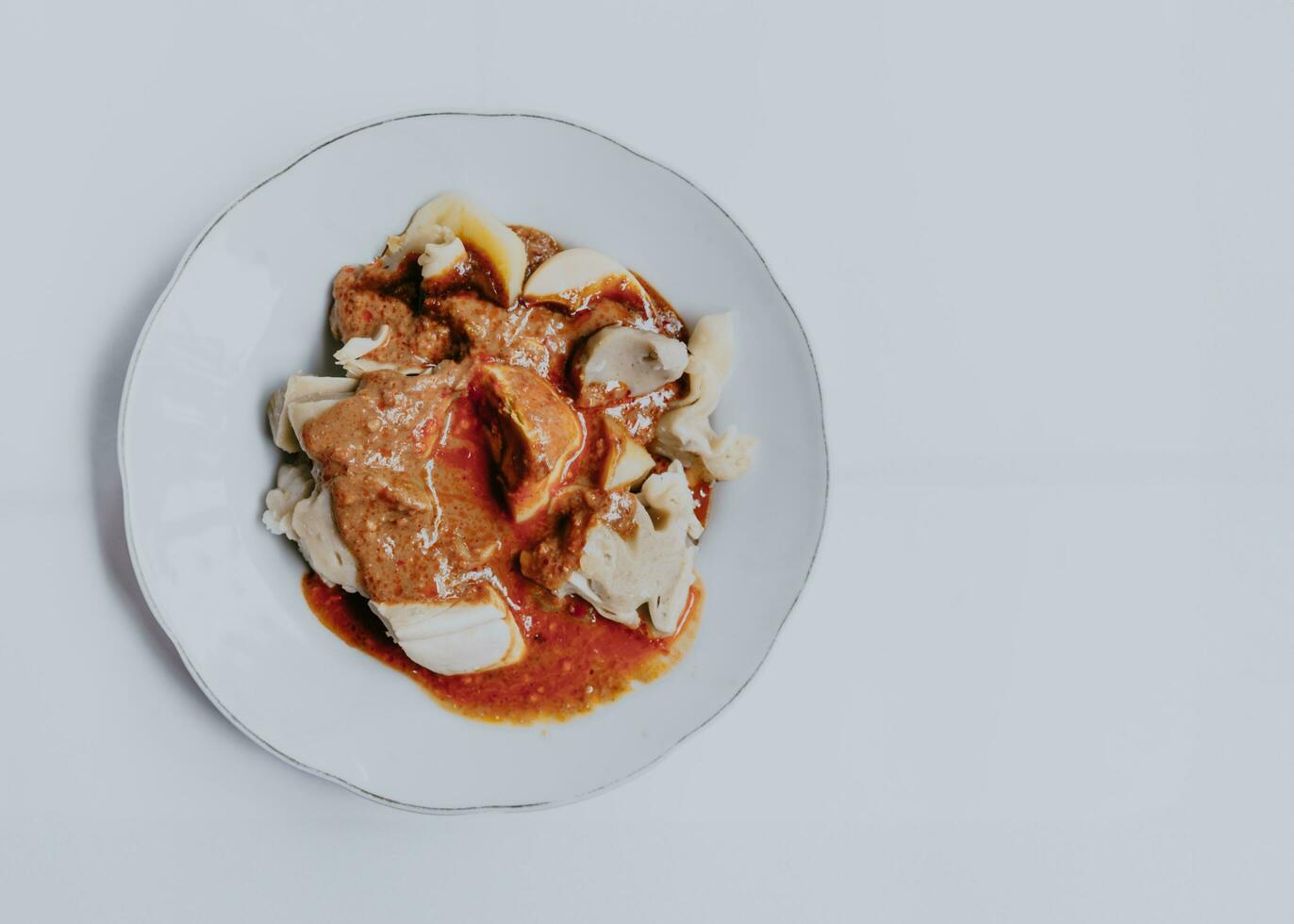 Top view of Siomay Bandung or steamed dumplings, traditional Indonesian street food with spicy peanut sauce and soy sauce served on a white plate. Copy space. Indonesian culinary food concept. photo