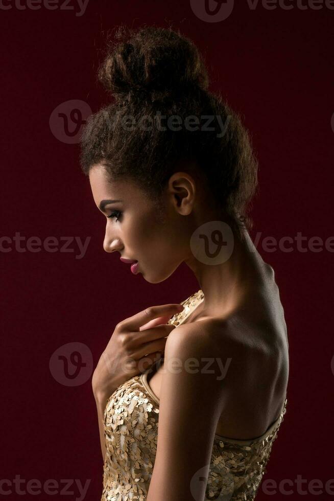 Moda joven africano mujer con constituir, en sexy oro vestido. foto