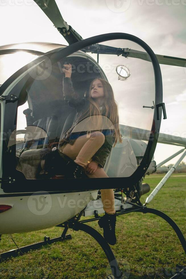 Preteen girl sitting in open cockpit of landed helicopter photo