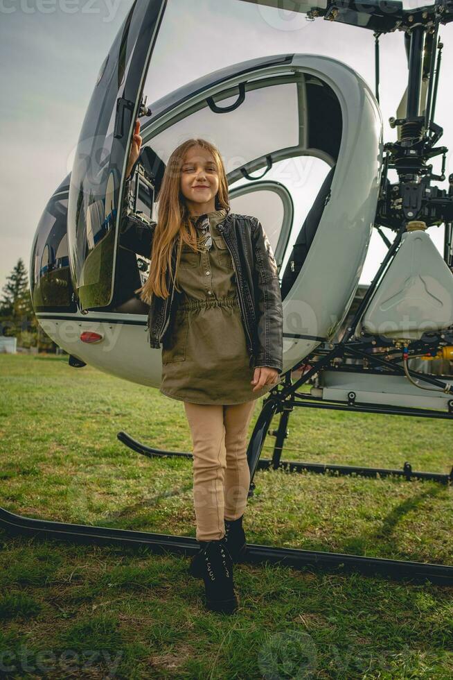 Smiling brown-haired preteen girl standing near helicopter photo