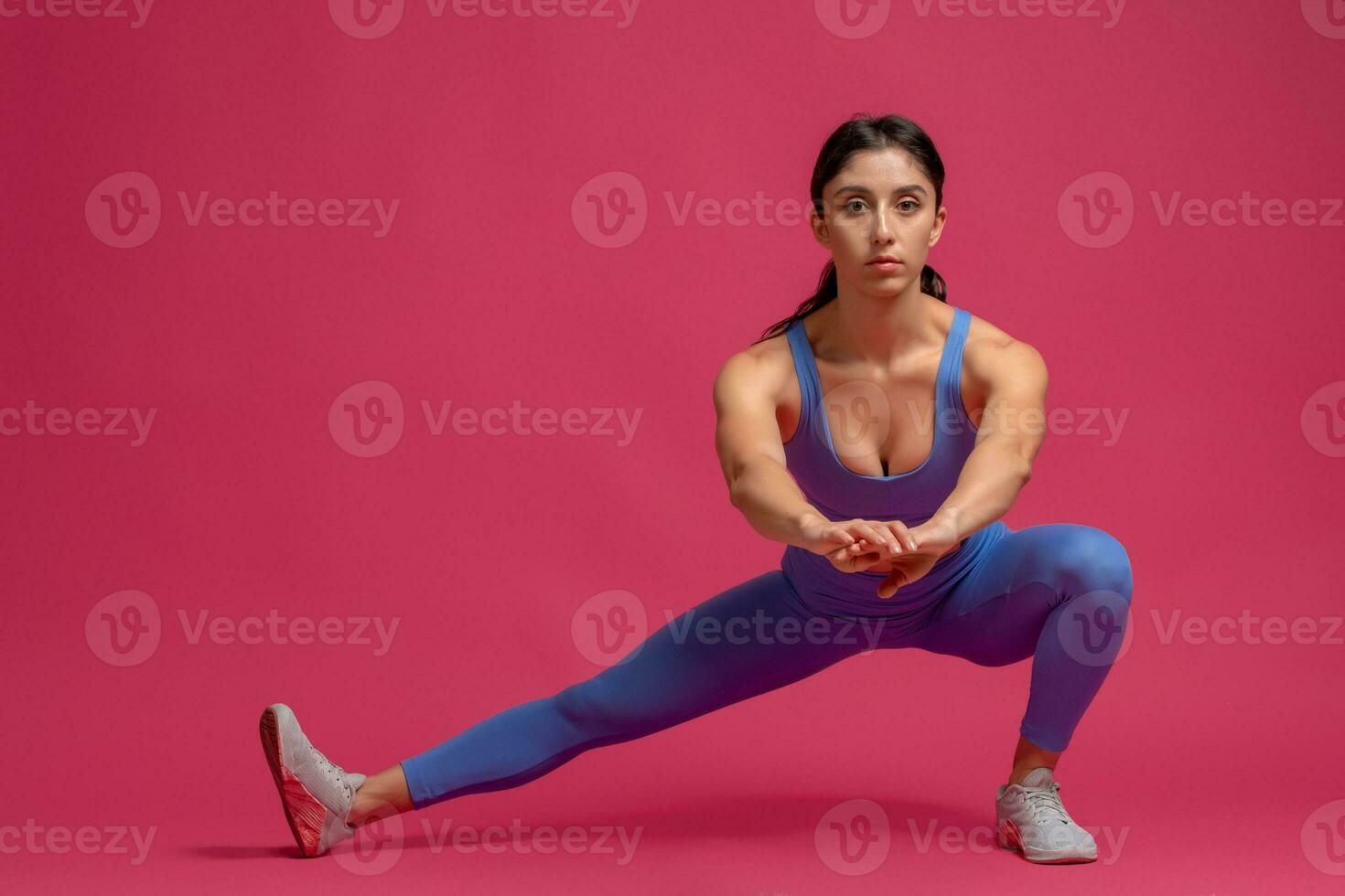Young woman performing bodyweight side lunges on maroon background photo