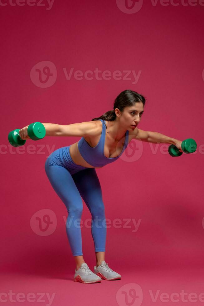 Athletic girl doing shoulders exercise on maroon background photo