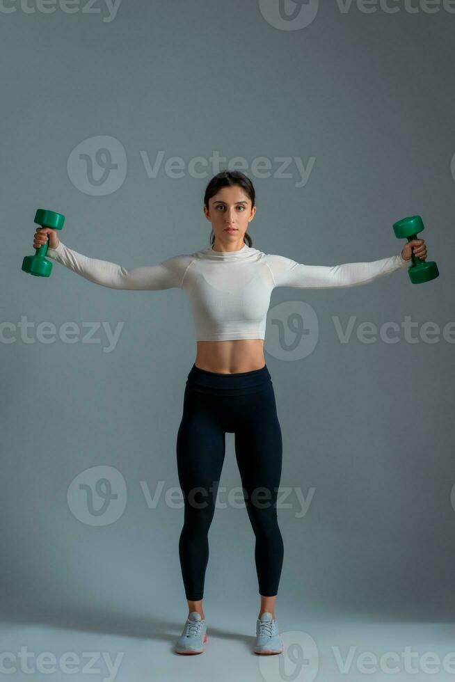 Girl performing set of shoulder exercises with dumbbells on grey background photo