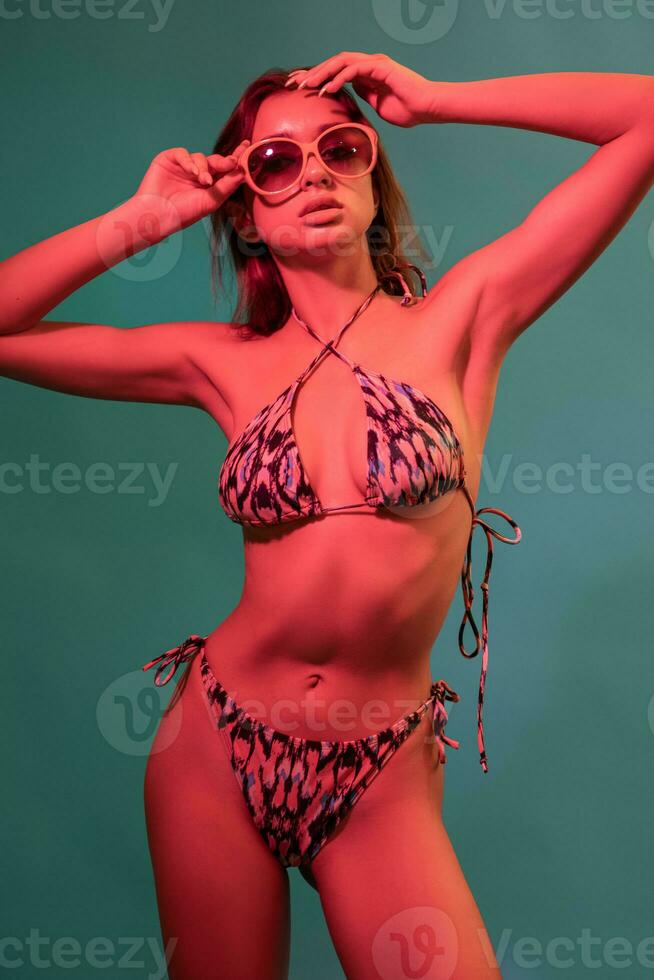 Young woman in swimsuit and sunglasses posing on blue background photo