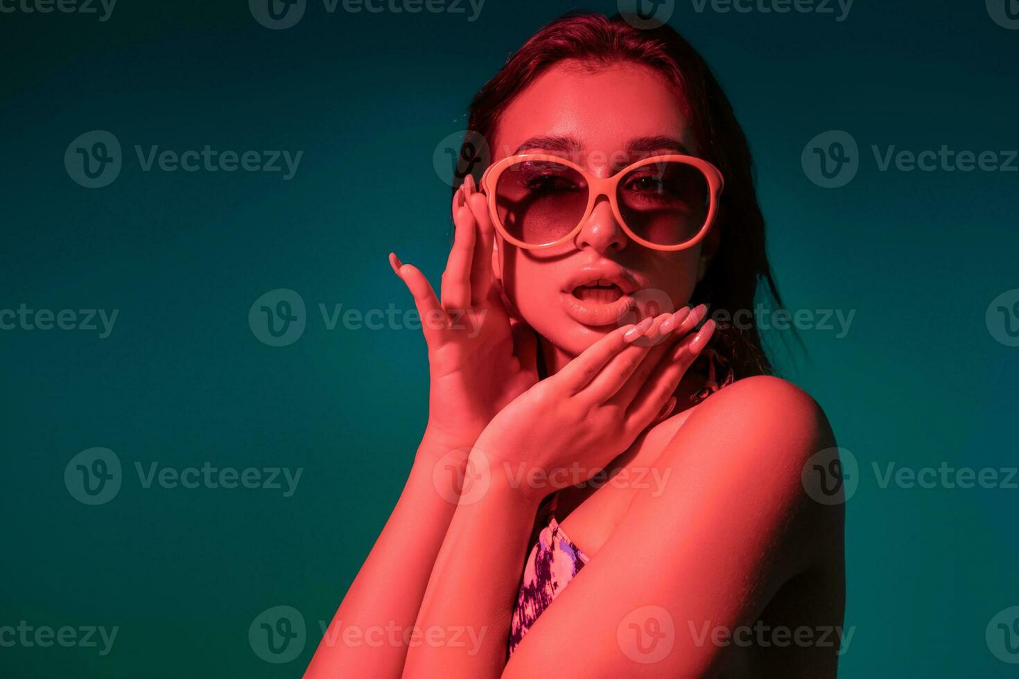 Surprised campy girl in swimsuit adjusting sunglasses on blue background photo