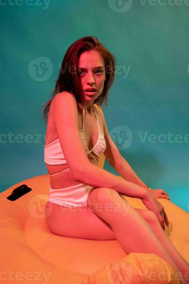 Girl in white swimsuit sitting on yellow inflatable pillow photo