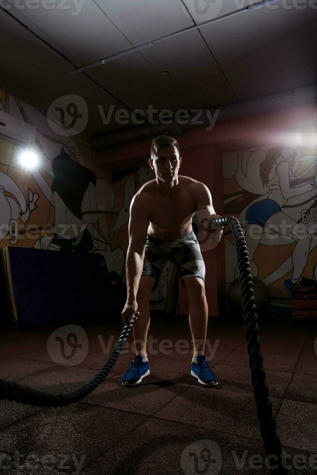 Young man working out with battle ropes at crossfit gym photo