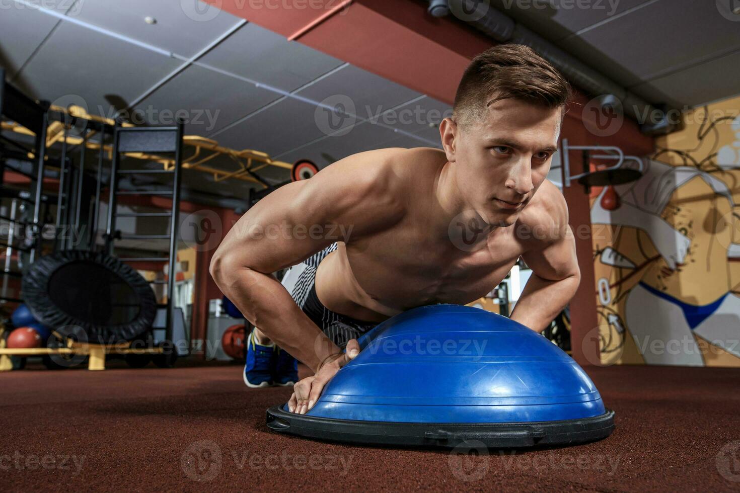 Muscular man doing push up on bosu ball at crossfit gym photo