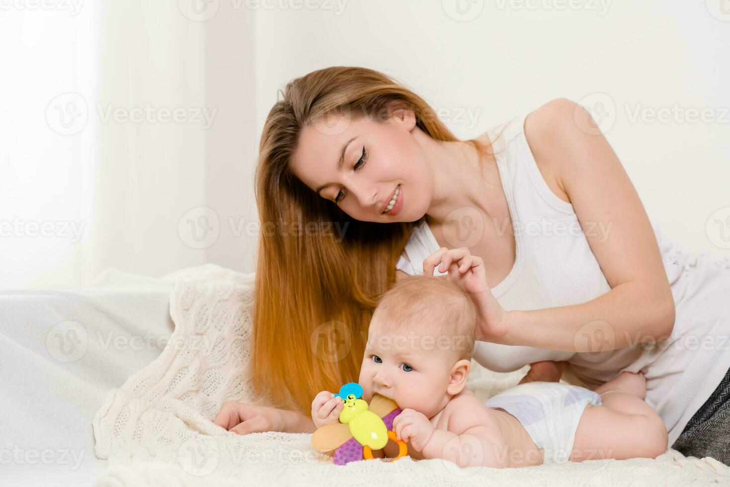 Mother and child on a white bed. Mom and baby girl in diaper playing in sunny bedroom. photo