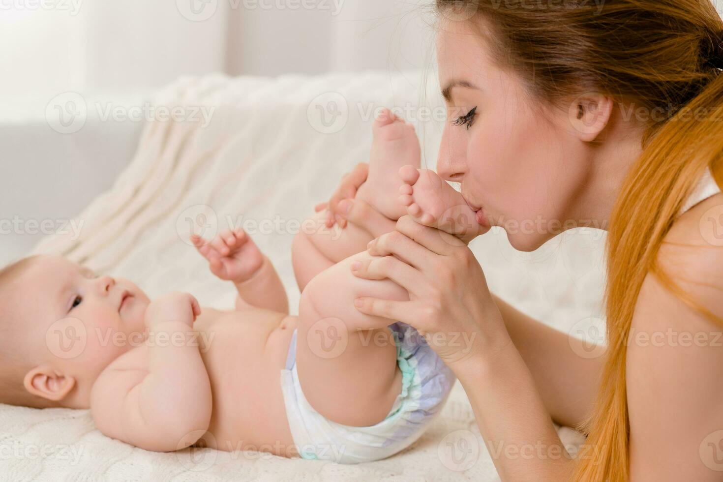 Mother and child on a white bed. Mom and baby girl in diaper playing in sunny bedroom. photo